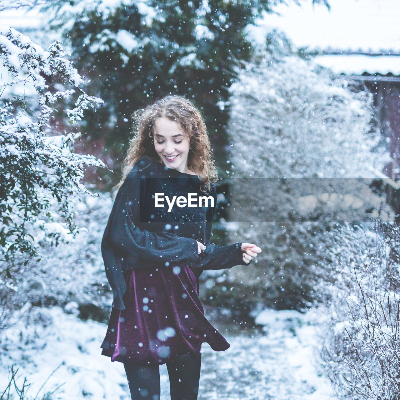 Smiling young woman with eyes closed standing on field during snowfall