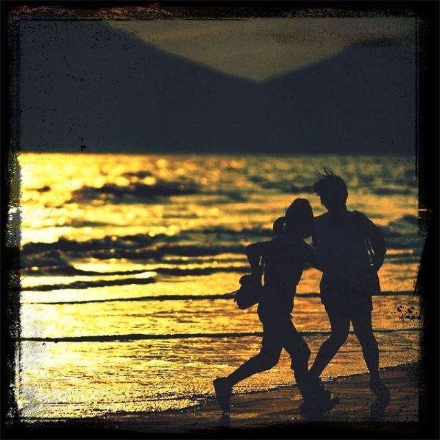 WOMAN STANDING ON BEACH AT SUNSET