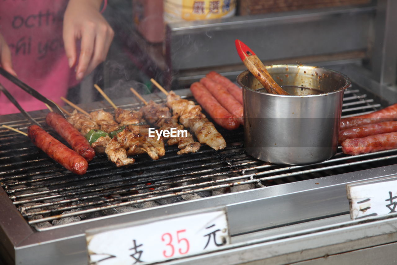 Midsection of person grilling sausages on barbecue grill at market stall