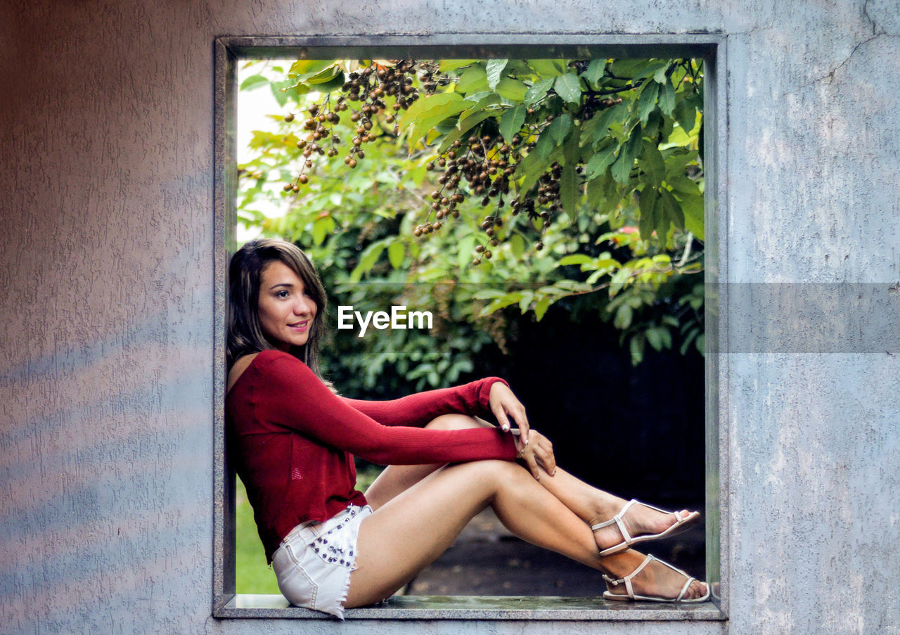 Side view full length of young woman sitting at window