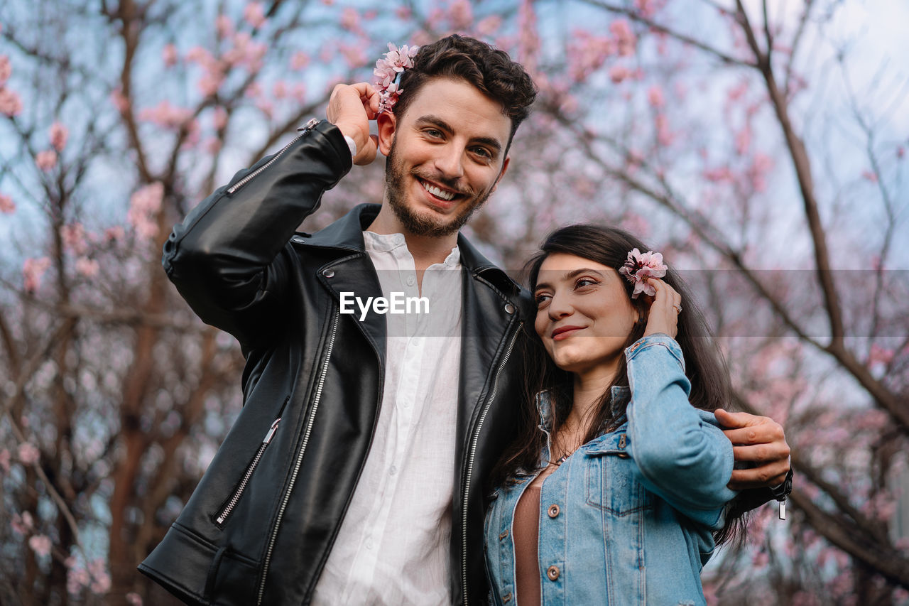 Young couple smiling in front of blooming trees in spring