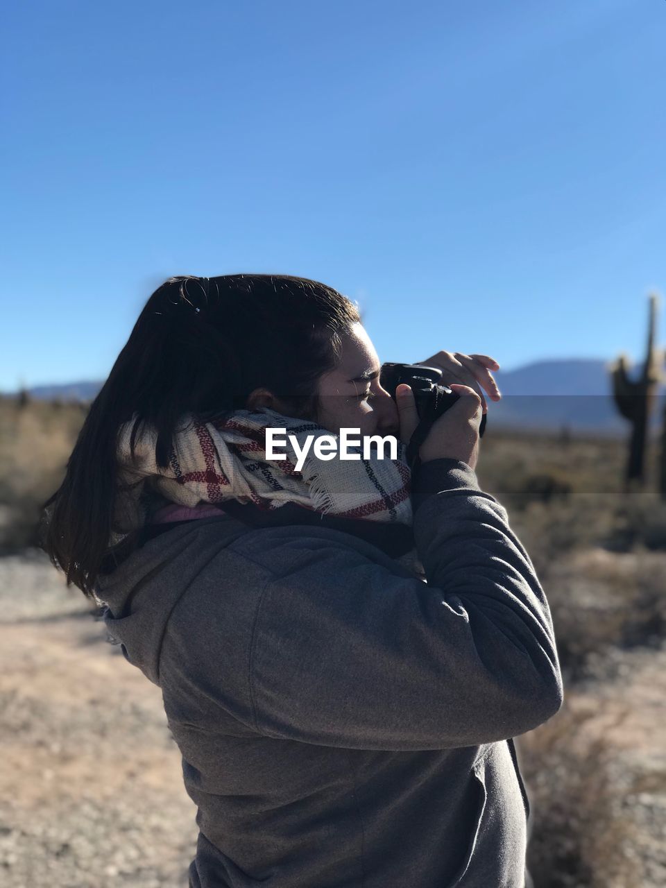 Side view of woman photographing from camera on land against clear sky