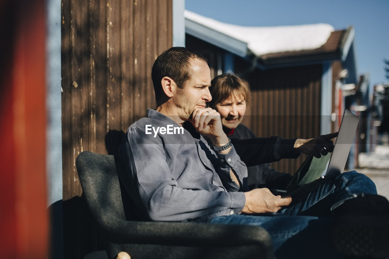 Female entrepreneur discussing over laptop with businessman while sitting against vacation home