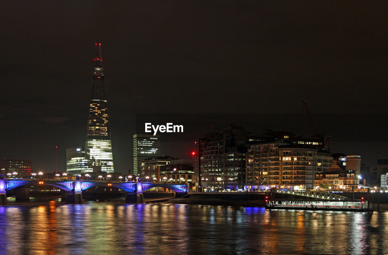 ILLUMINATED BUILDINGS BY RIVER AT NIGHT