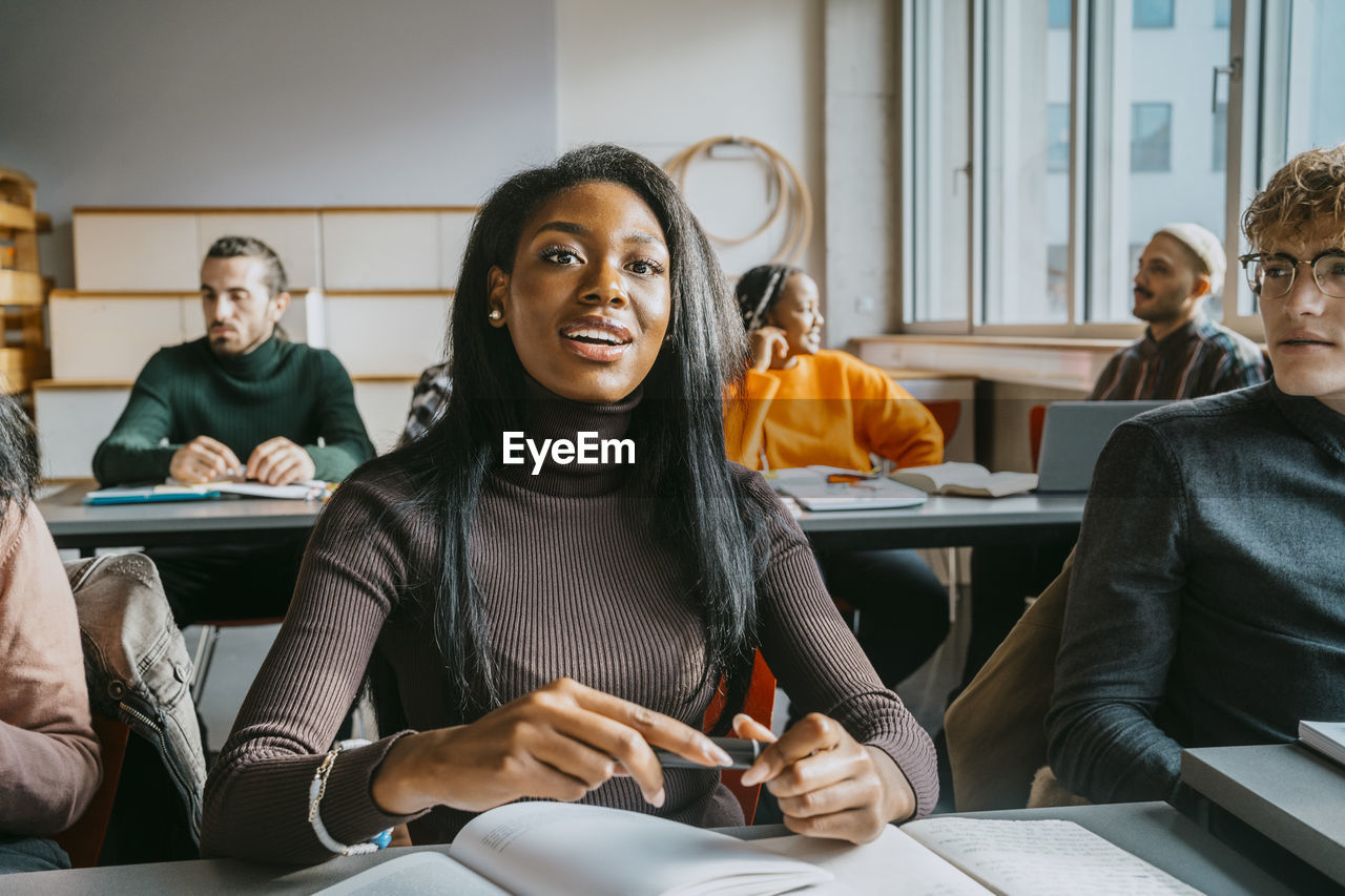 Young female student sitting with friends in classroom of university