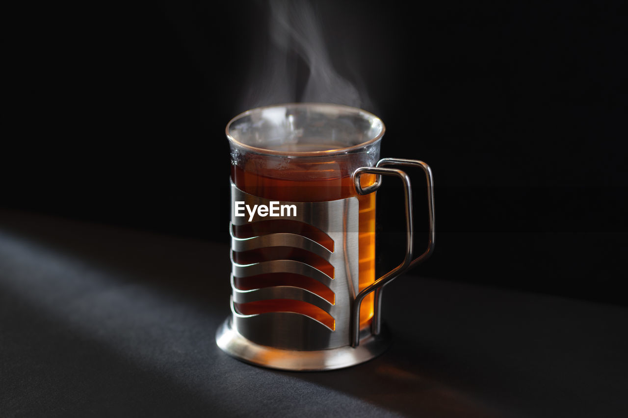 A cup of hot black tea in glass with rising steam in sunlight in cozy dark atmosphere