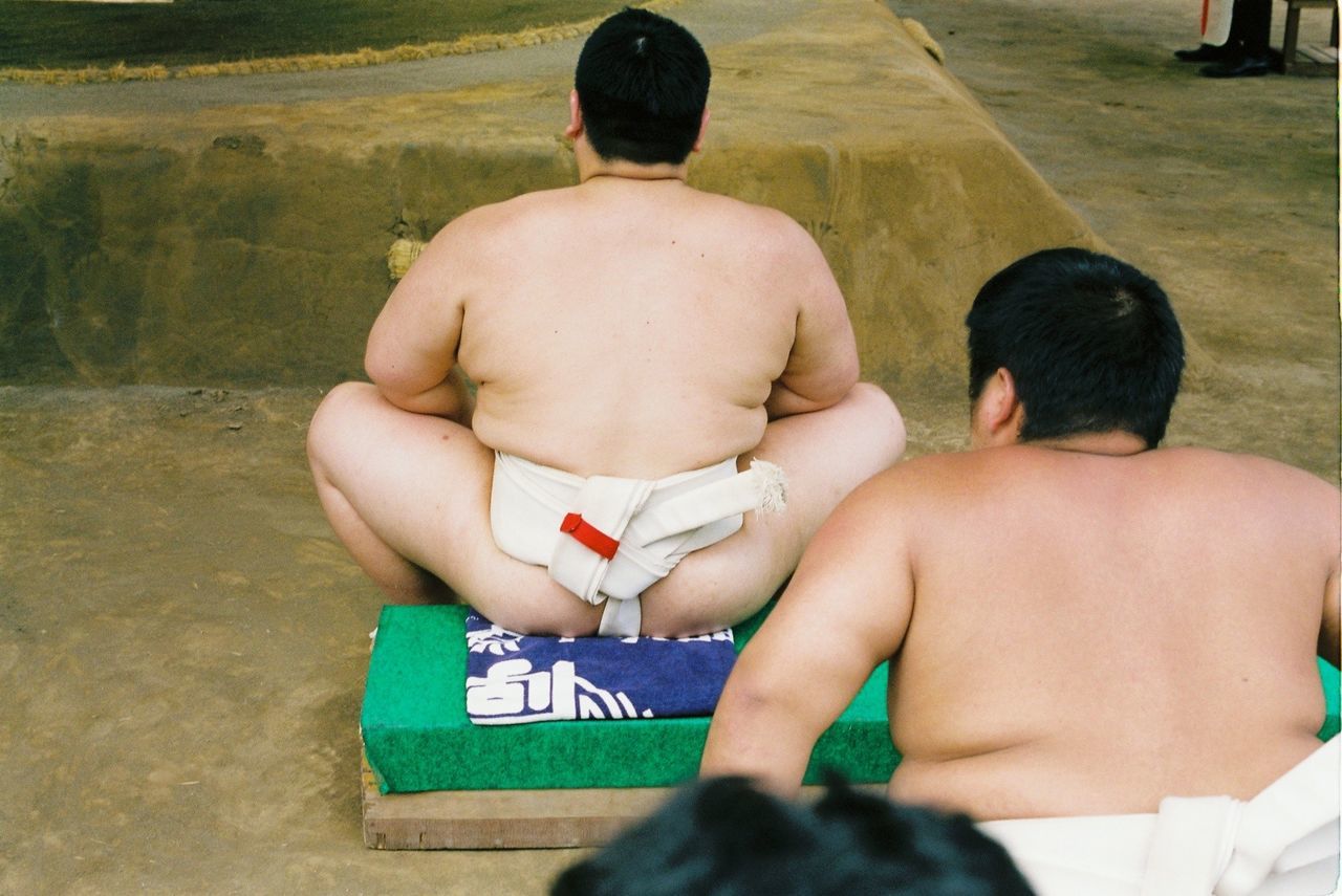 REAR VIEW OF SHIRTLESS BOY SITTING ON TABLE