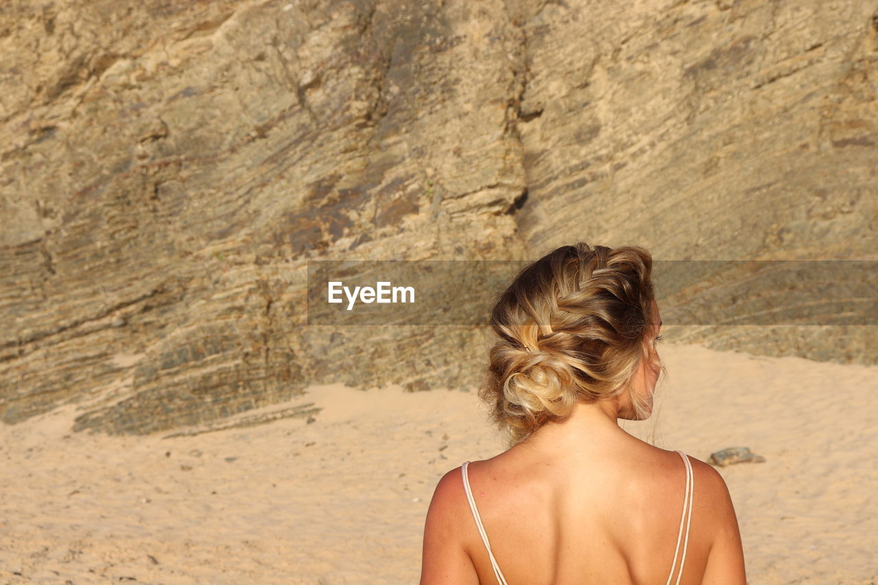 REAR VIEW OF WOMAN STANDING AGAINST ROCK