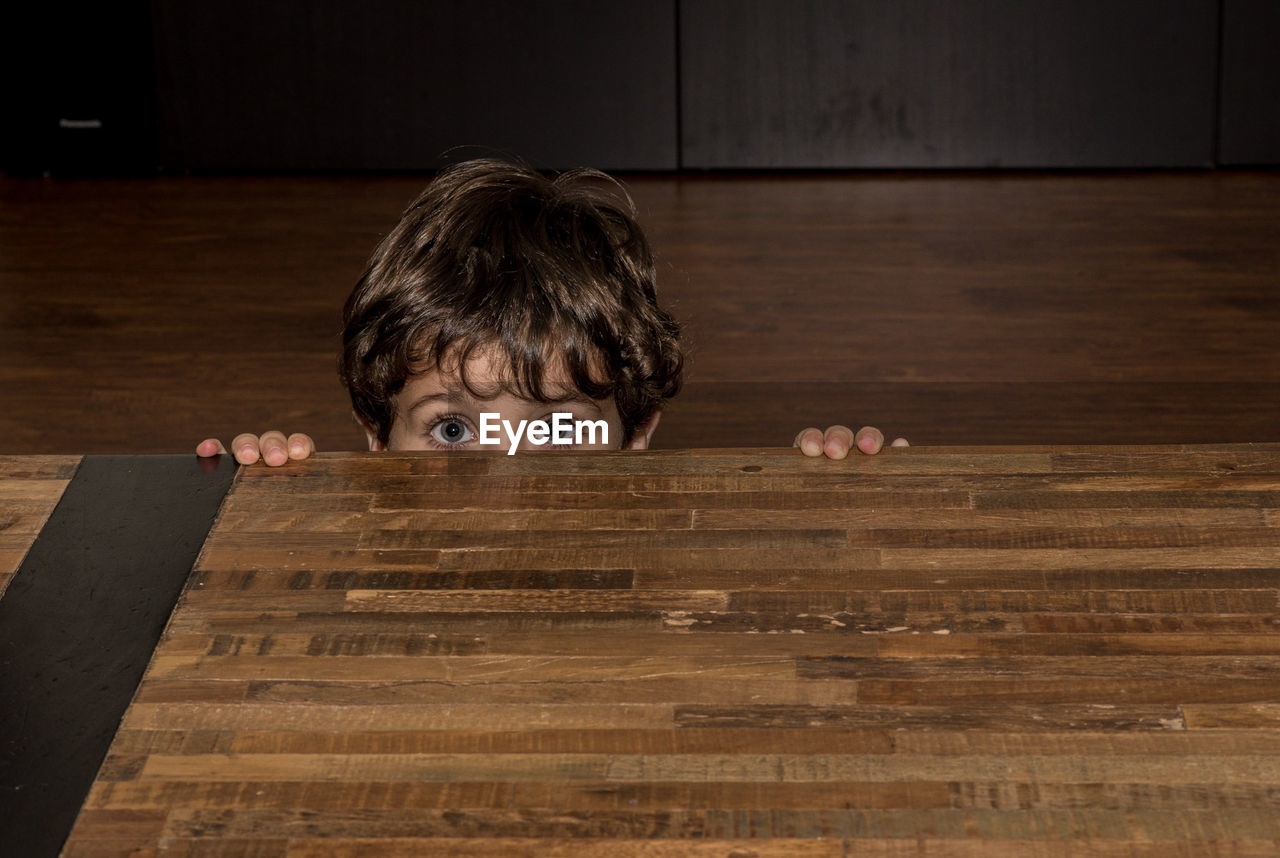 Portrait of boy hiding behind wooden table