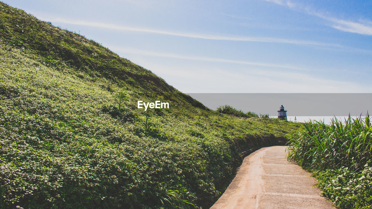 Scenic view of pathway leading to lighthouse against cloudy sky