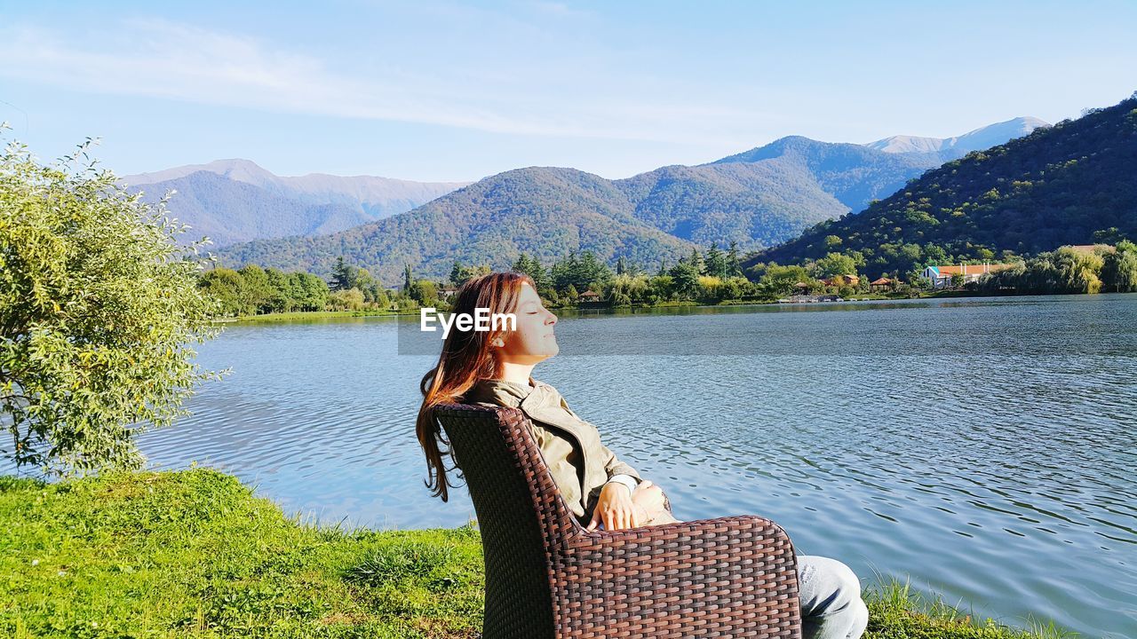 Young woman with eyes closed relaxing by lake