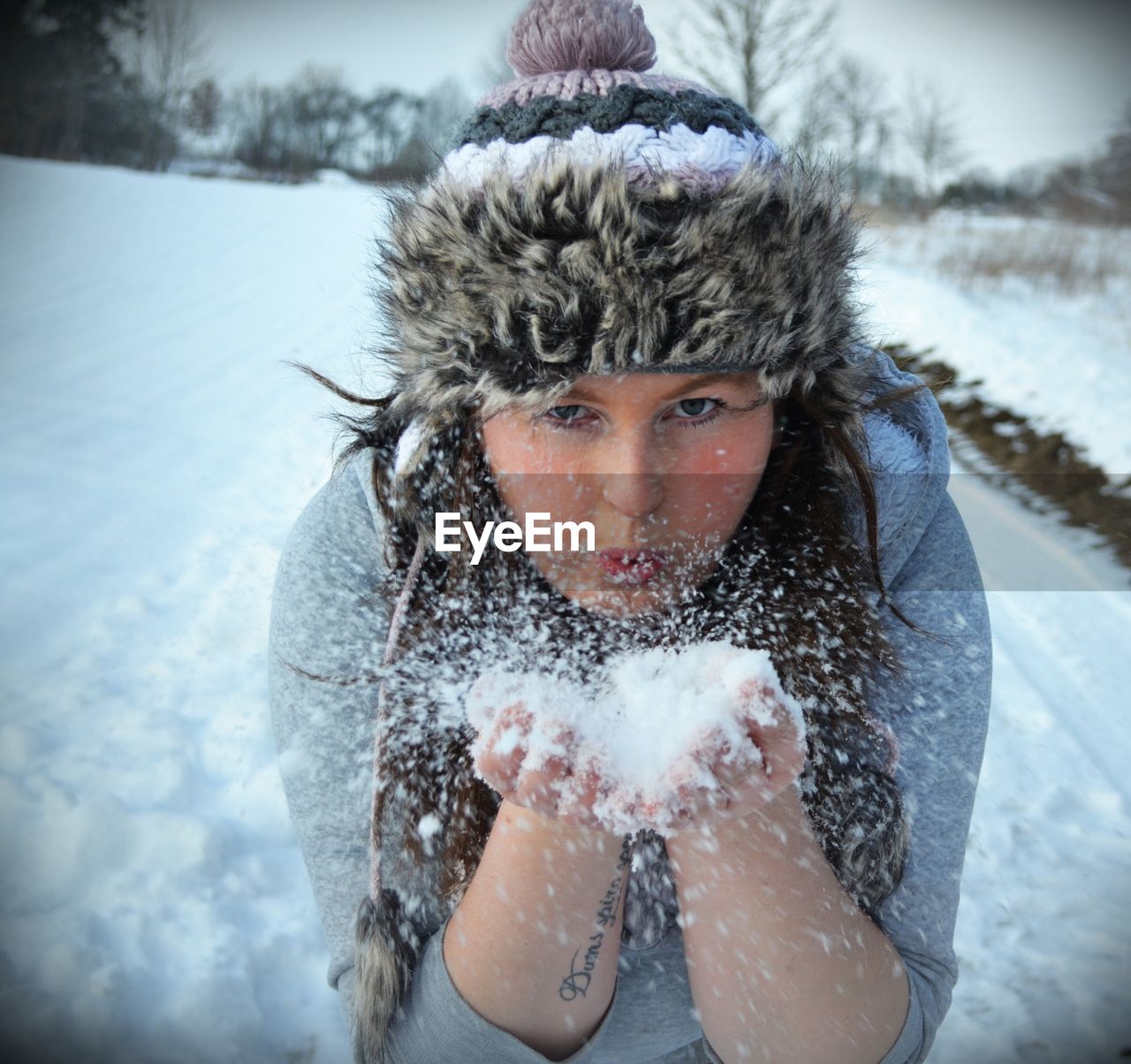 Close-up portrait of young woman blowing snow on field