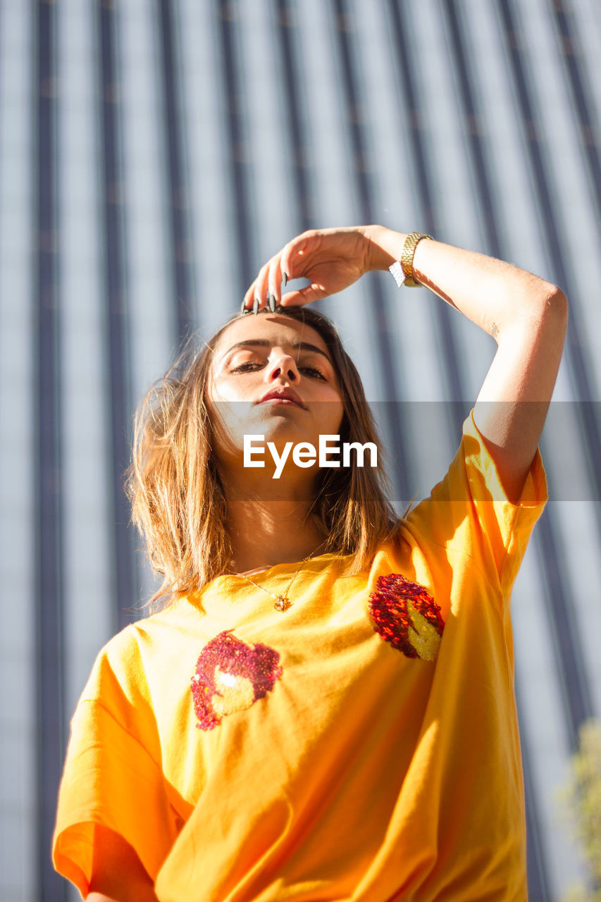 Low angle portrait of young woman standing against building