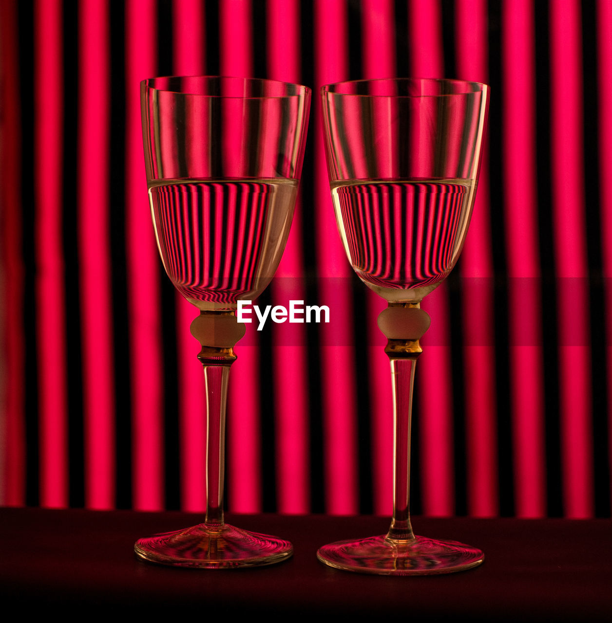 Close-up of wineglasses on table against red curtain