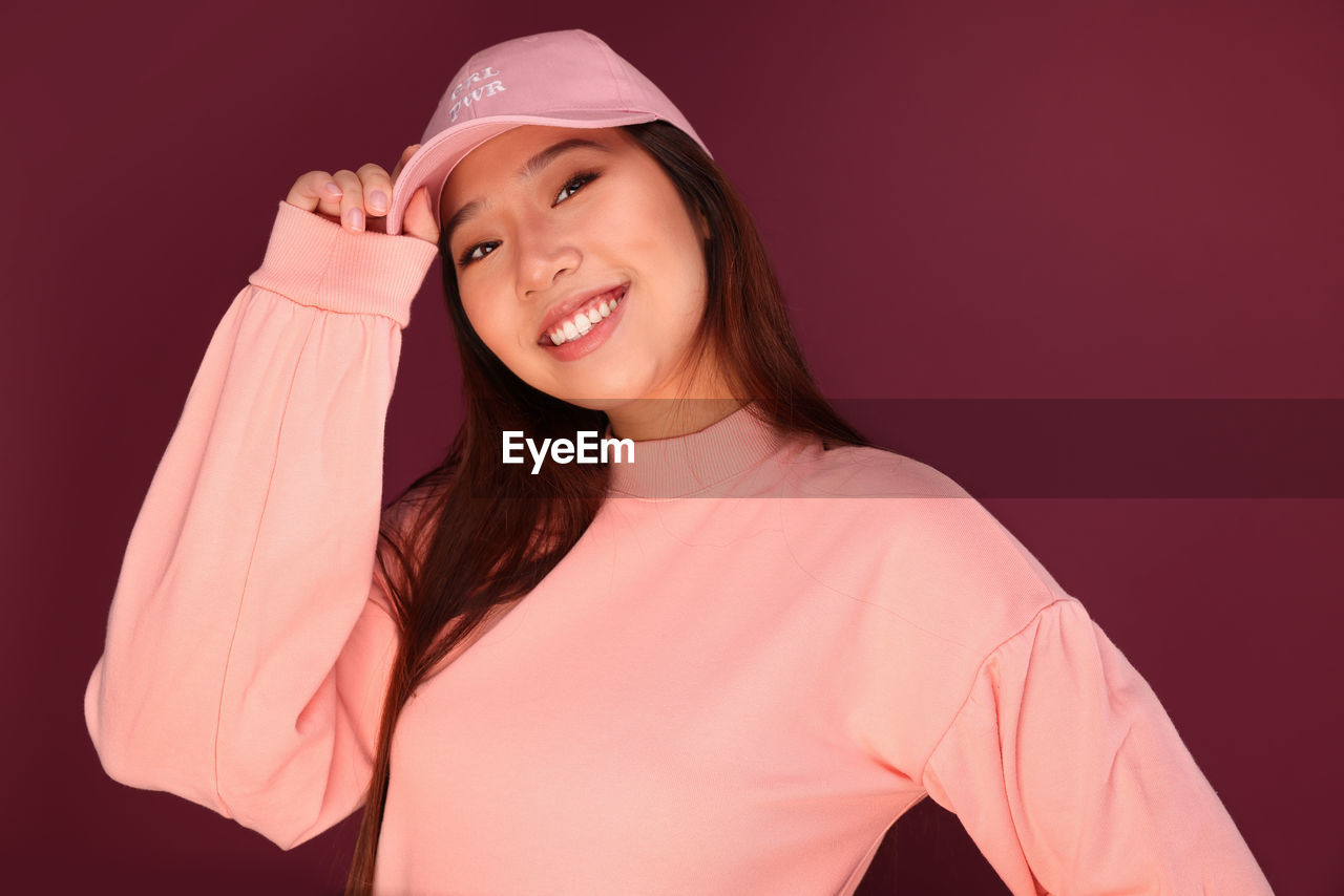 Portrait of happy young asian woman in the studio wearing pink clothes over garnet background
