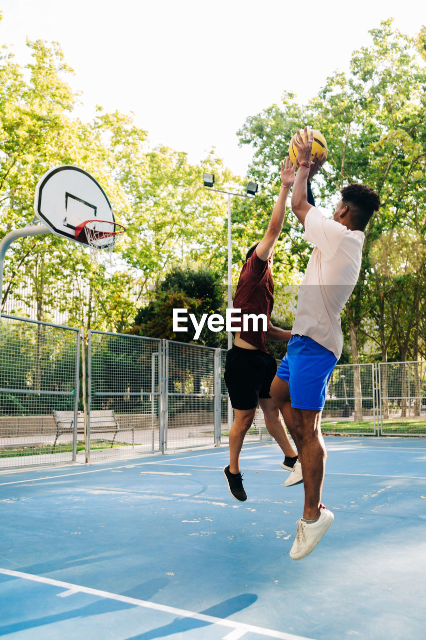 Ethnic african american friends players running together with ball while playing basketball on sports ground in sunny day