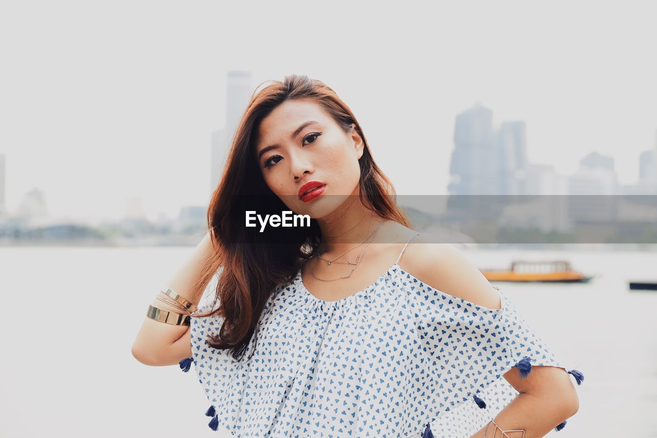 Portrait of young woman standing against river in city