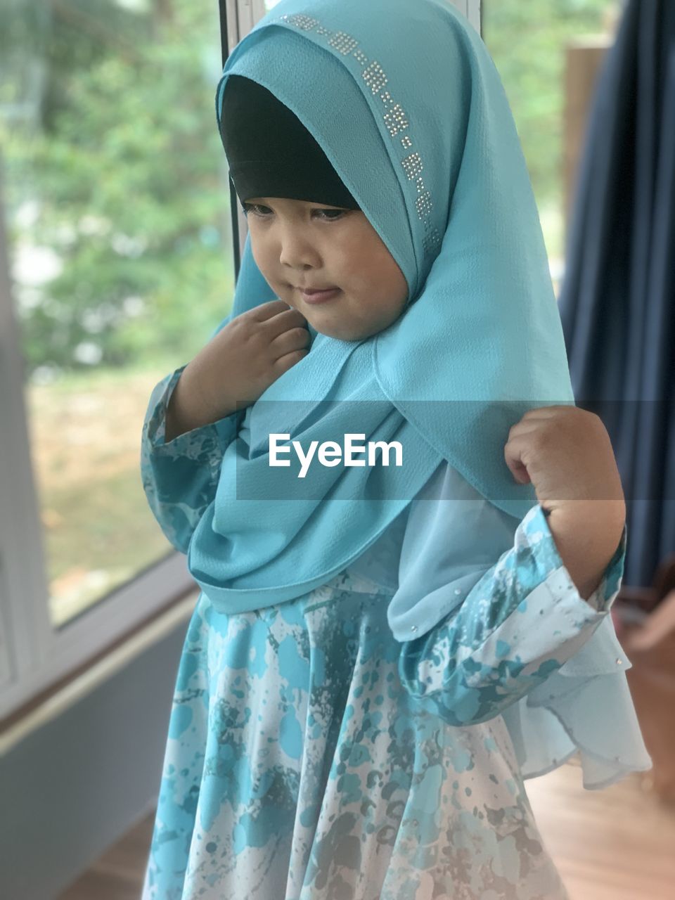 one person, clothing, child, blue, childhood, costume, standing, hijab, traditional clothing, headscarf, women, dress, looking, day, emotion, window, female, adult, lifestyles, outdoors, portrait, men, veil, waist up, focus on foreground, three quarter length, person
