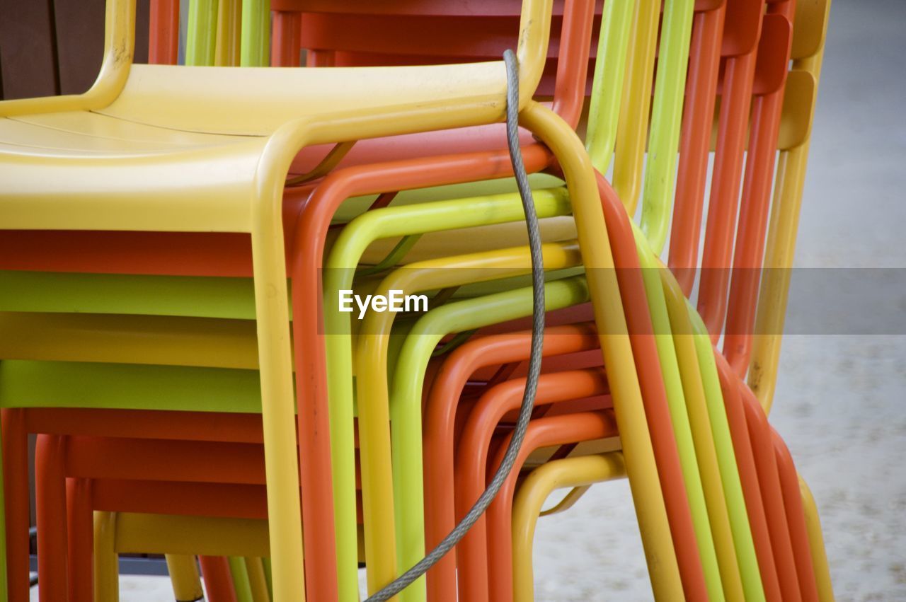 CLOSE-UP OF MULTI COLORED CHAIRS IN ROW AGAINST YELLOW WATER