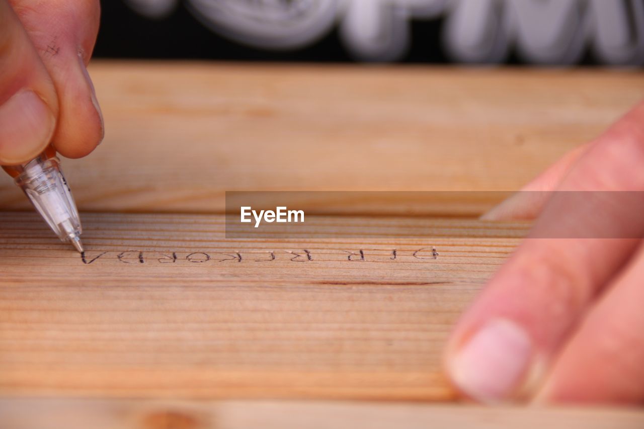 Close-up of hand writing with pen on wood