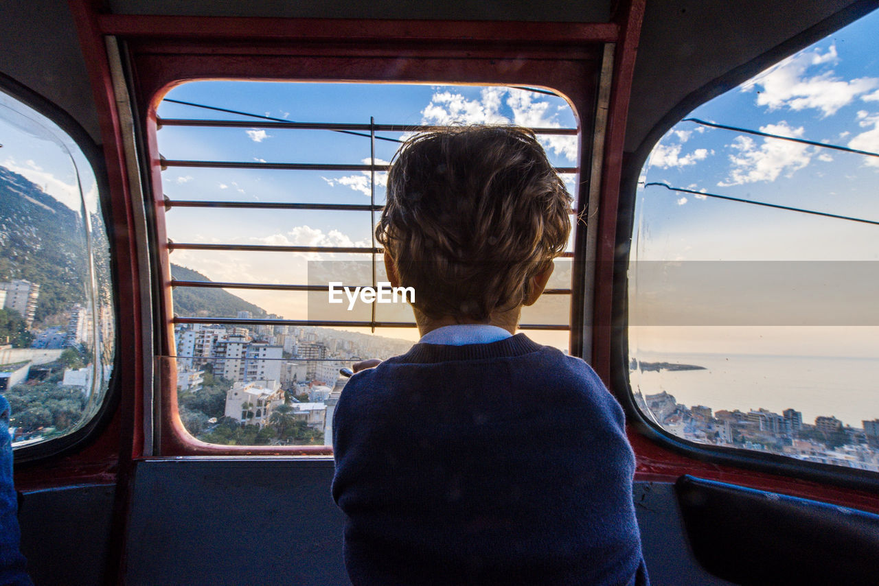 Rear view of boy looking through cable car window