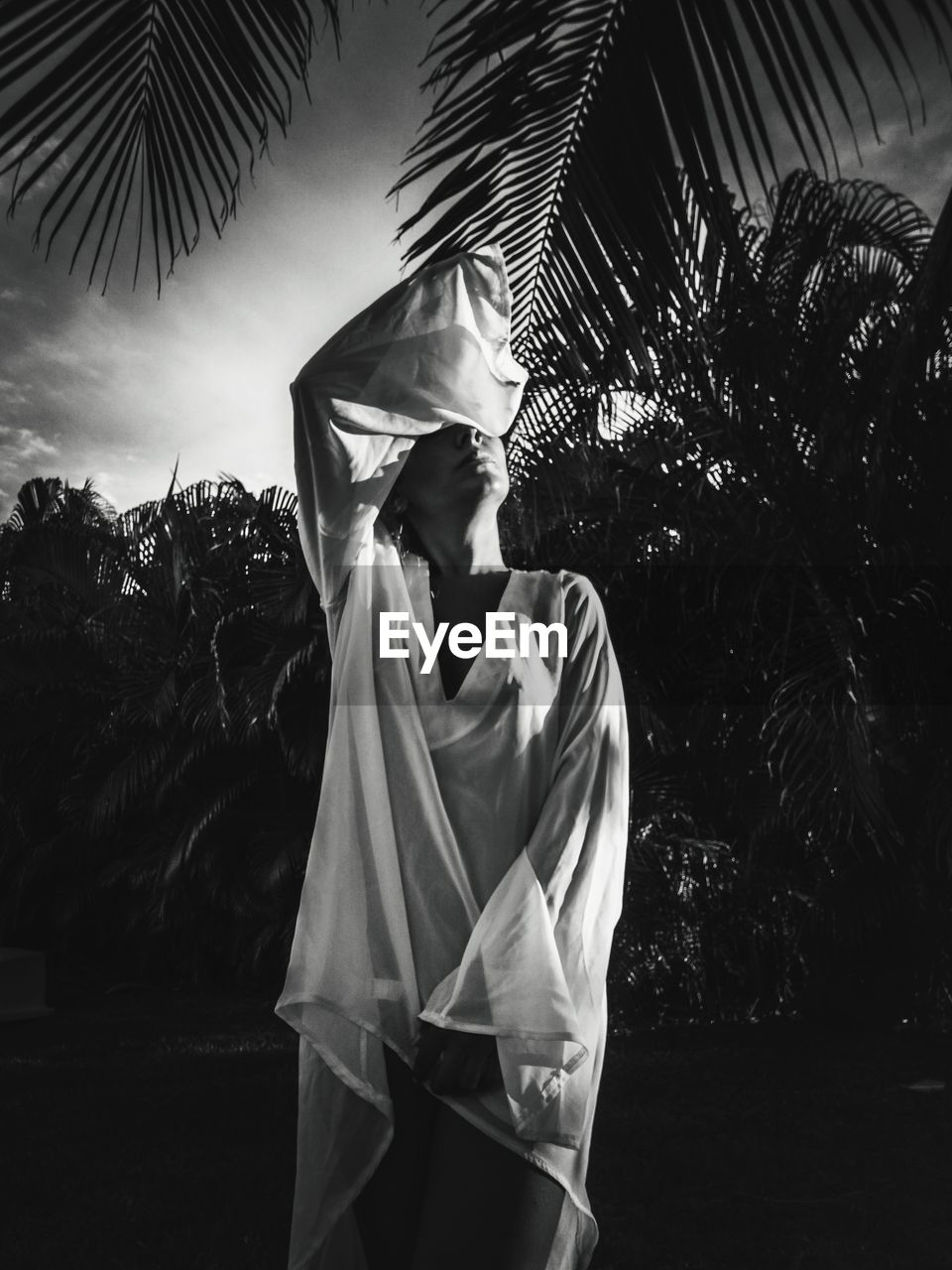 Woman covering eyes while standing by palm trees