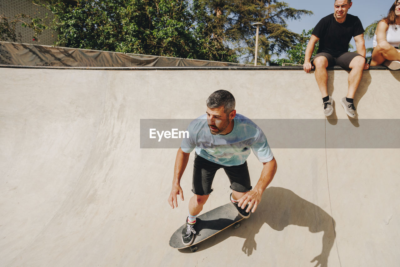 Man skateboarding on sports ramp with friends in background