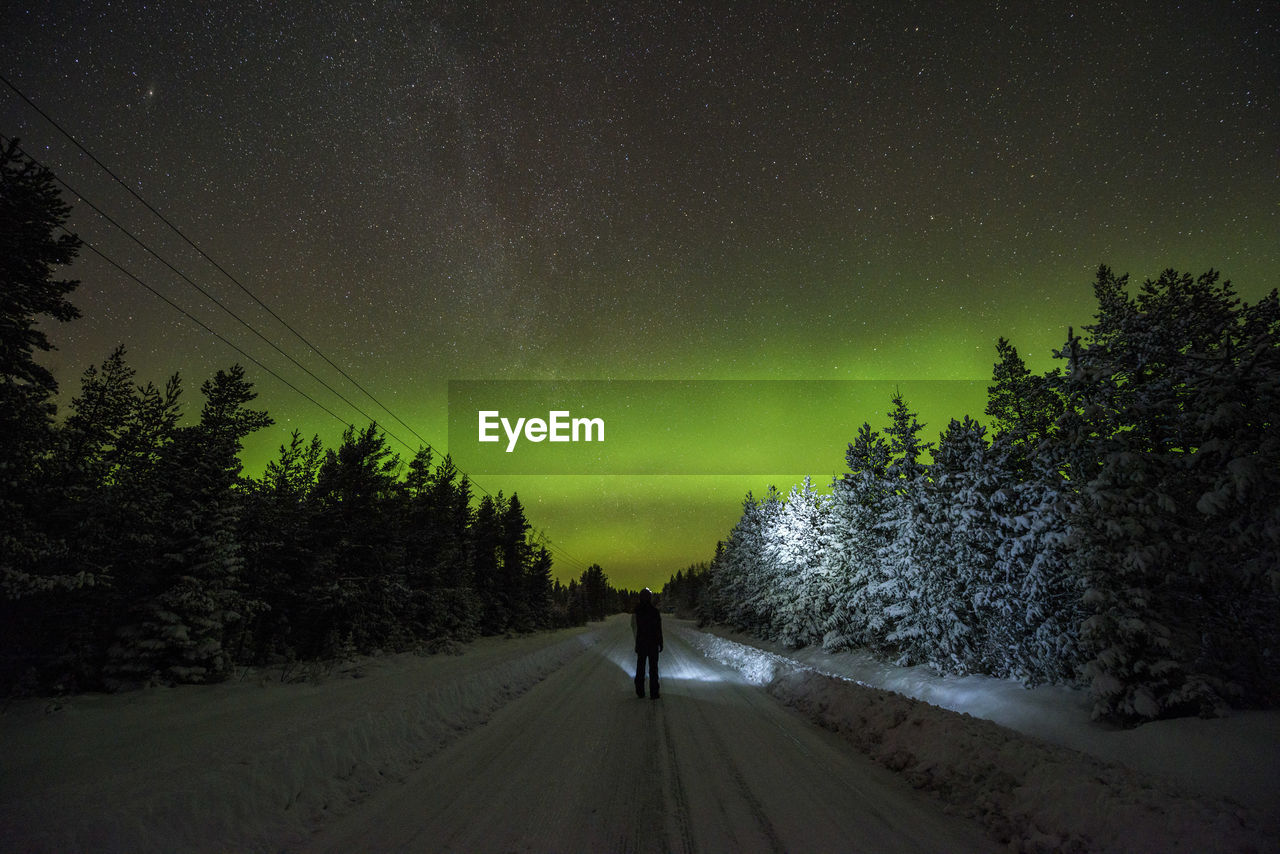 Man walking on road amidst trees against star field at night