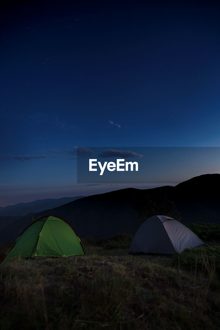 tent, camping, night, sky, star, landscape, scenics - nature, environment, nature, adventure, land, travel destinations, travel, beauty in nature, mountain, exploration, no people, tranquility, tourism, moonlight, trip, space, holiday, vacation, astronomy, outdoors, tranquil scene, blue, dark, light, darkness, grass, horizon, non-urban scene, space and astronomy, long exposure, science