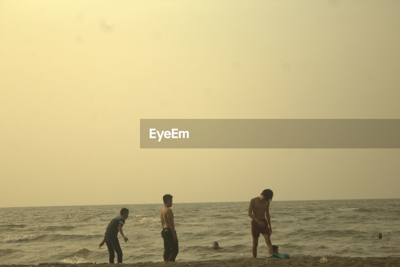 PEOPLE ON BEACH AGAINST CLEAR SKY DURING SUNRISE