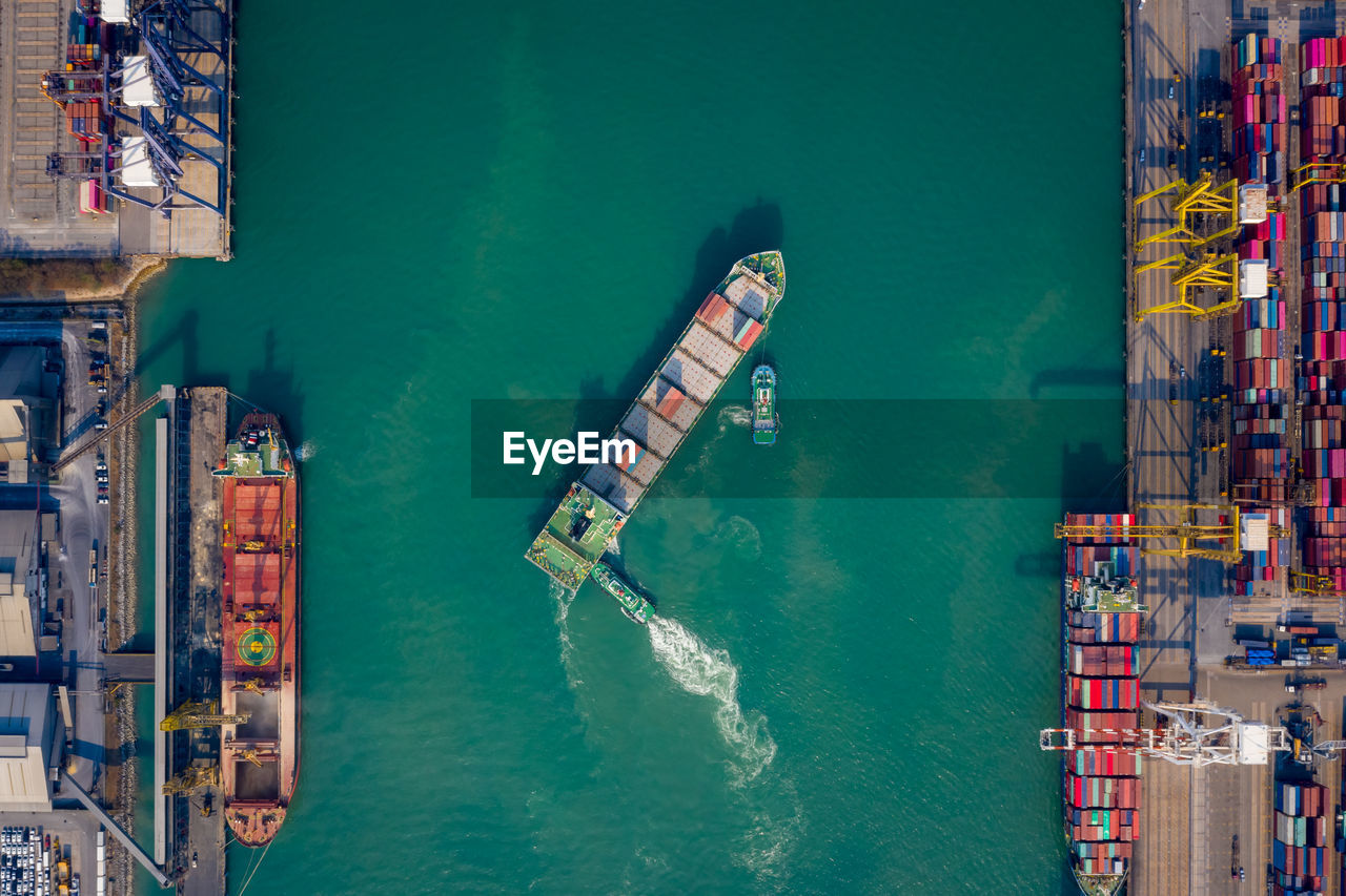 Aerial top view tugboat pushing container ship to quayside for load/unload container via crane 