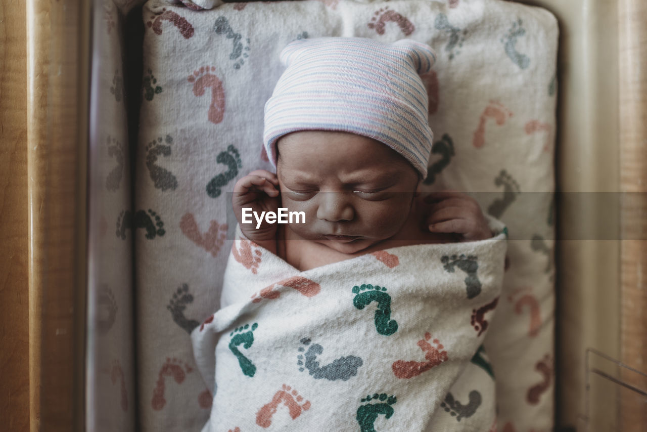 Overhead view of newborn boy with hat in hospital bassinet