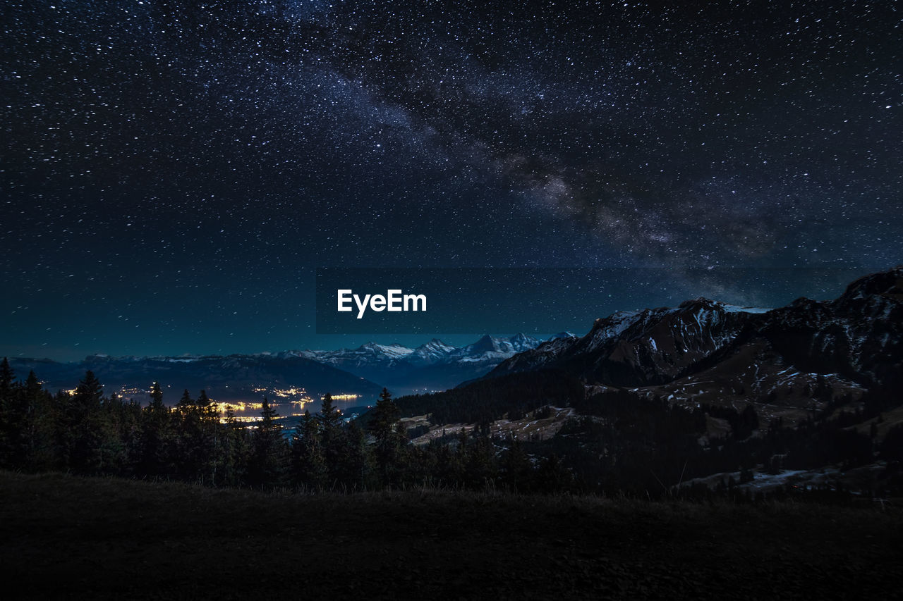 Scenic view of landscape and mountains against star field at night