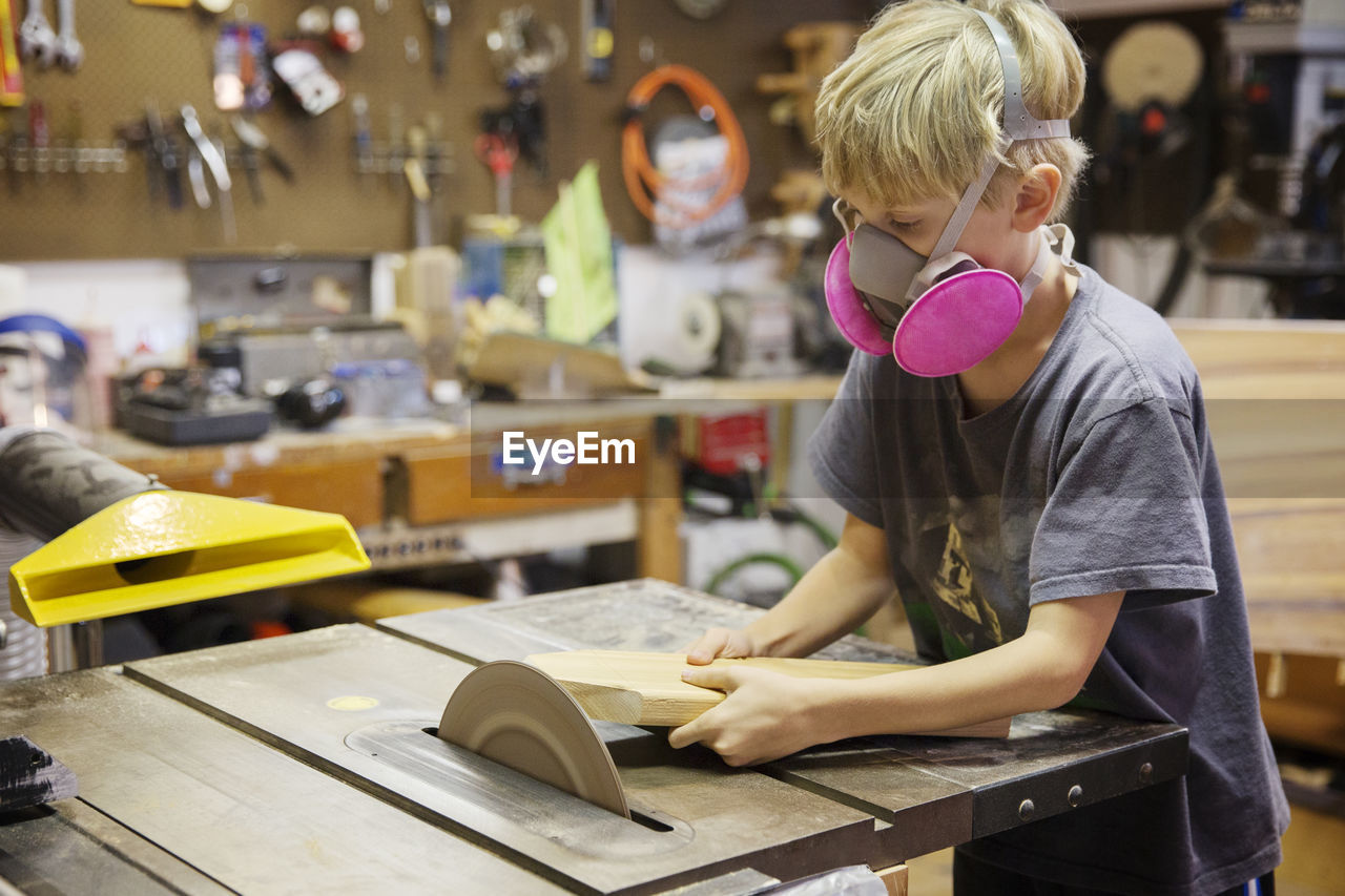 Boy cutting wood with table saw in workshop