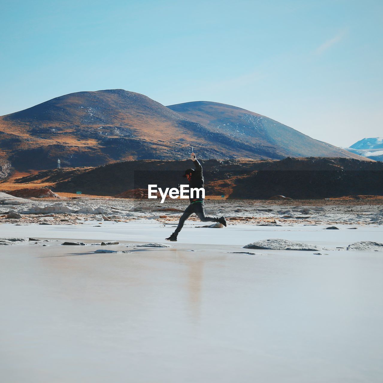 Side view of man jumping over salt lake on sunny day