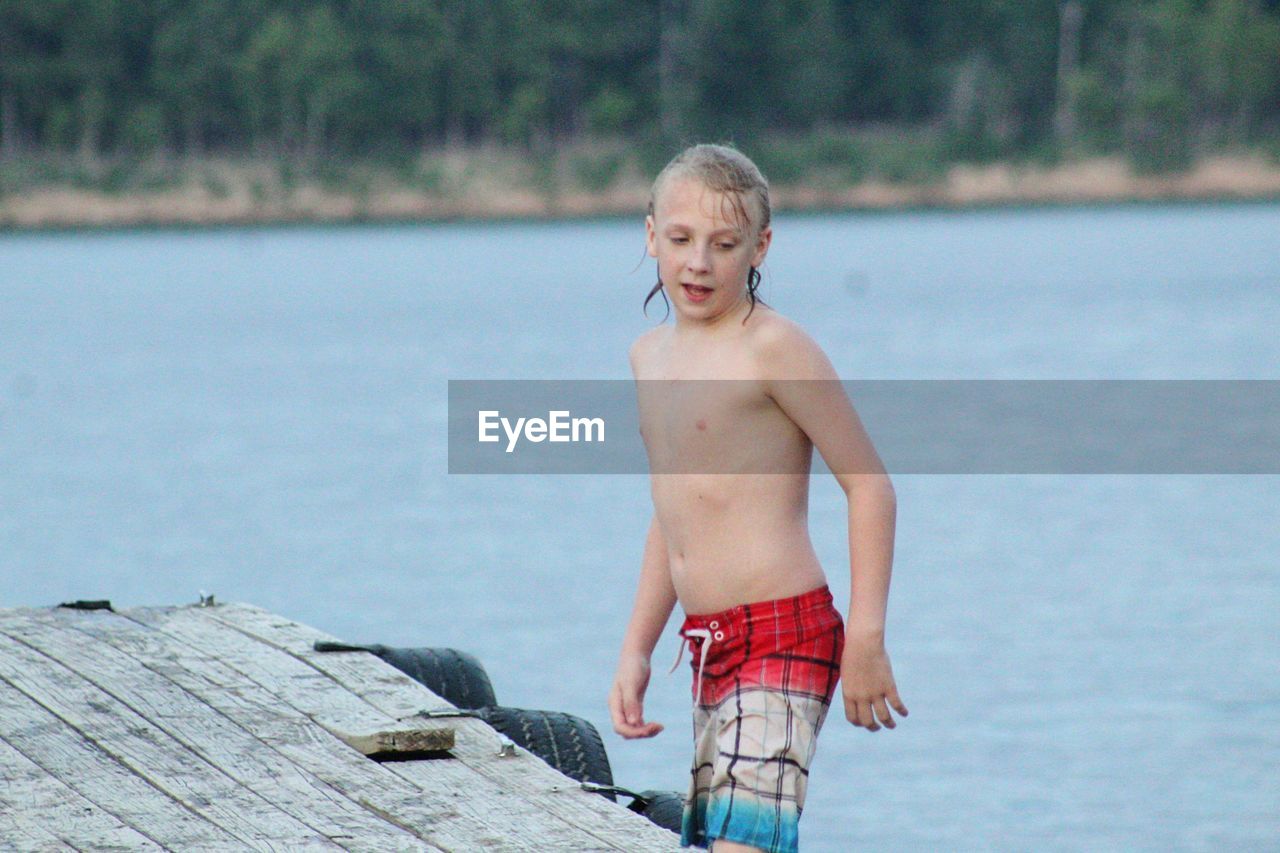 Shirtless boy standing on pier over lake