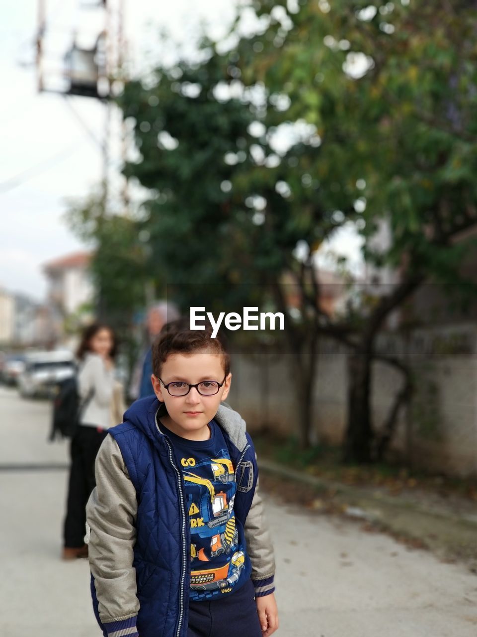 Portrait of boy standing on street against trees