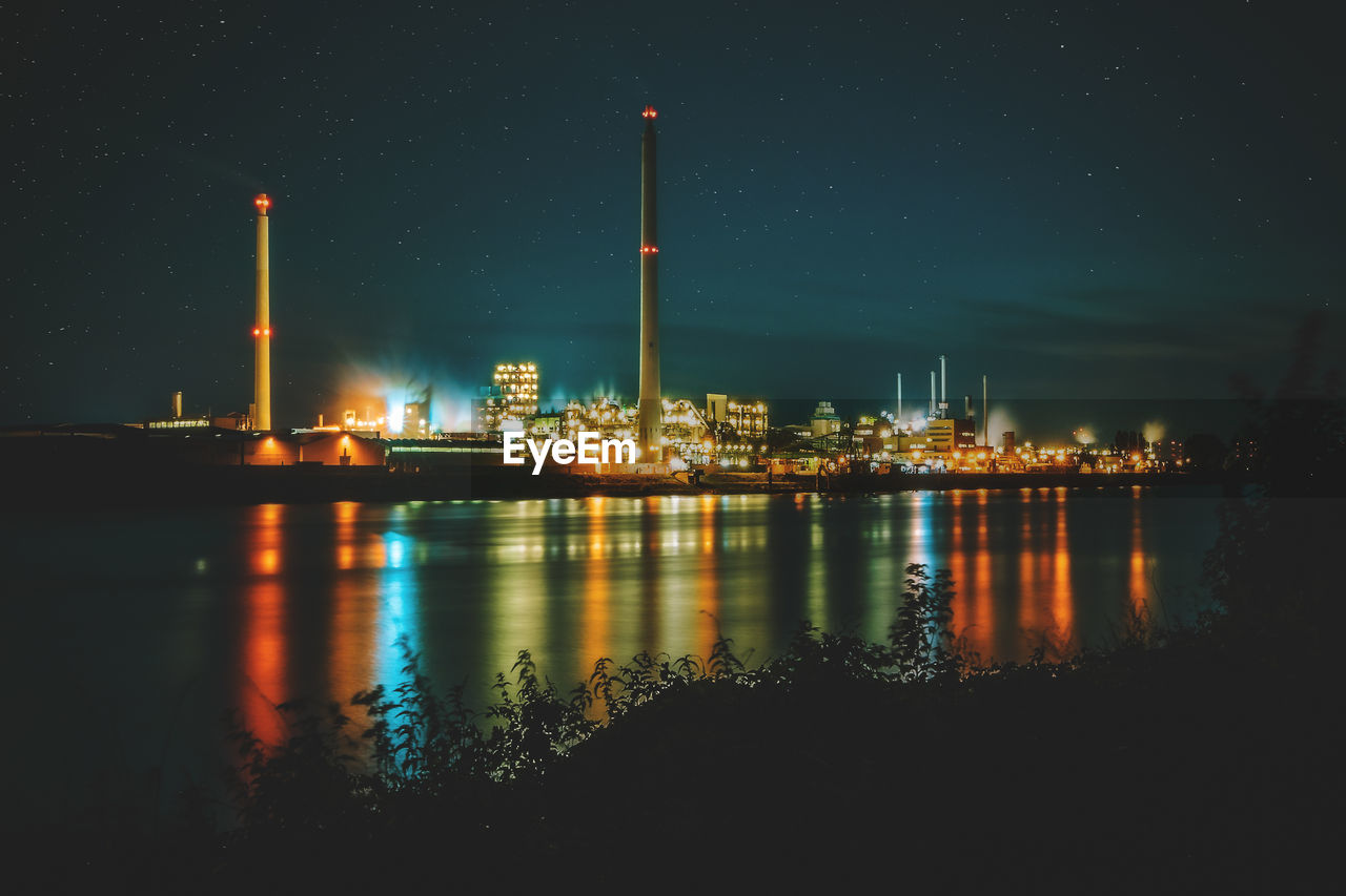 Illuminated city by river against sky at night