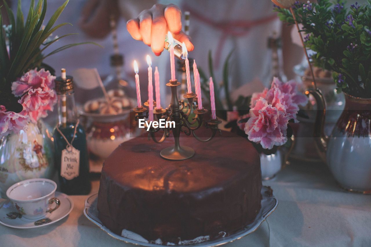 Cropped hand lighting candles on chocolate cake