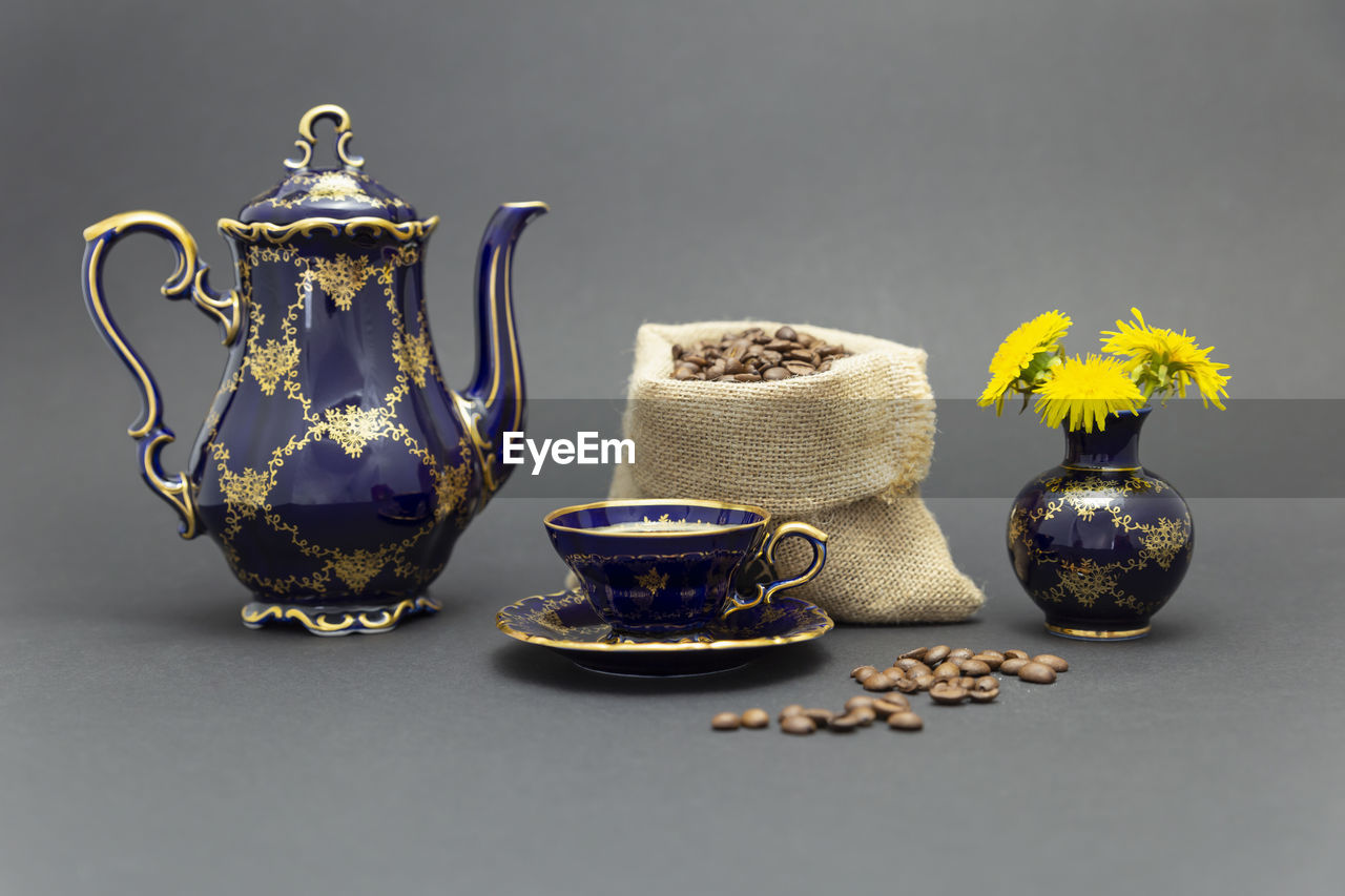 Still life with a blue vintage porcelain coffee set, a flower vase and a sack with coffee beans.