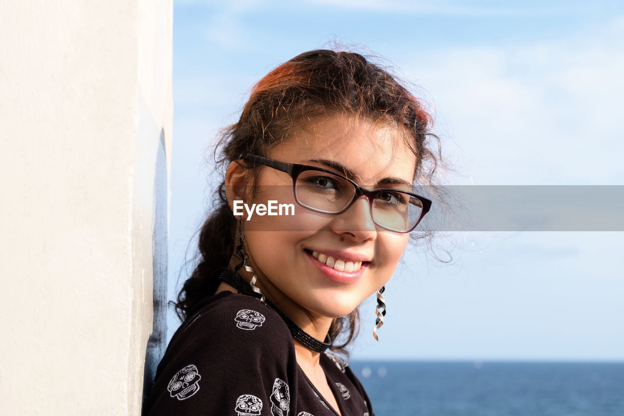 Portrait of smiling young woman wearing eyeglasses with sea in background