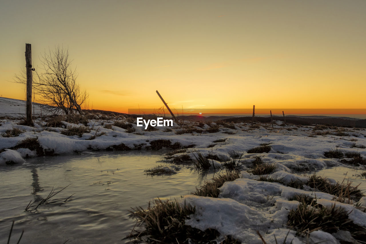 SNOW COVERED LAND AGAINST SKY DURING SUNSET
