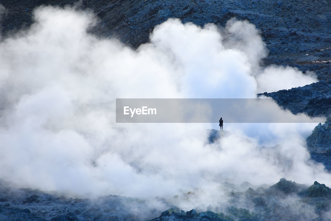 Scenic view of clouds by rock formation with person standing