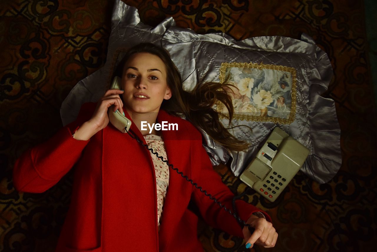 Portrait of young woman talking on telephone while lying on bed