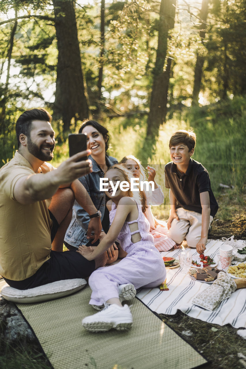 Father taking selfie with family through smart phone during picnic