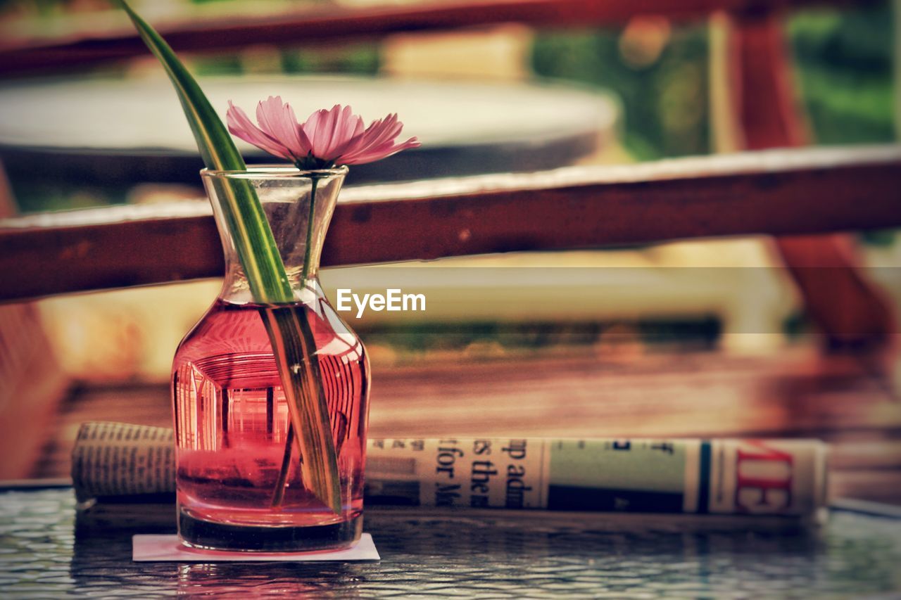 CLOSE-UP OF RED FLOWER IN GLASS ON TABLE