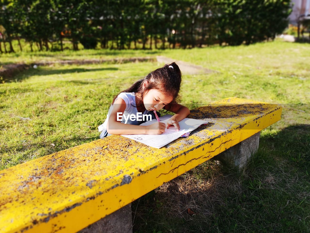 High angle view of girl doing homework on table while sitting in park