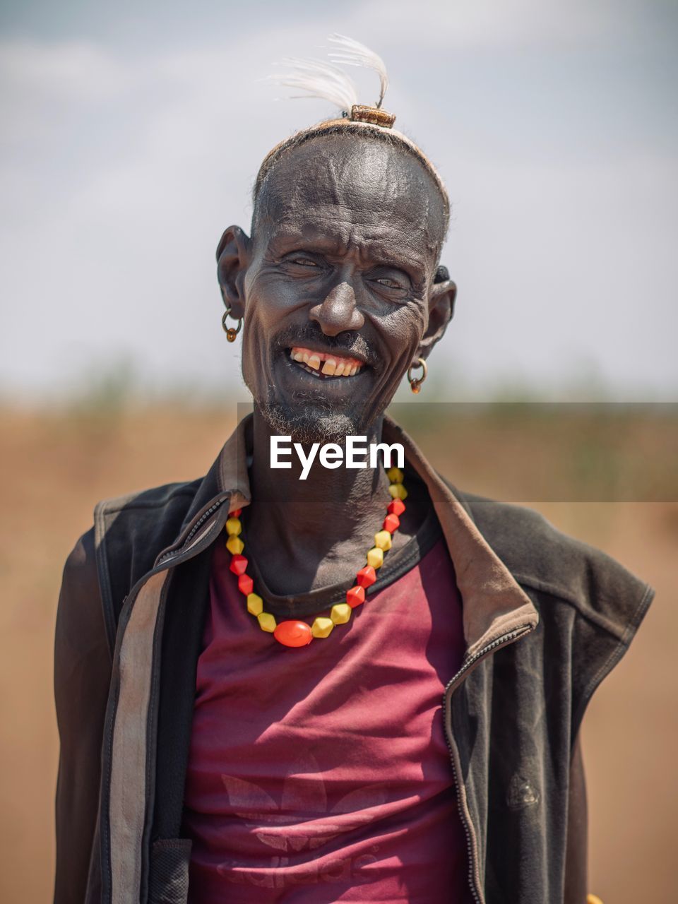 PORTRAIT OF SMILING YOUNG MAN STANDING ON OUTDOORS