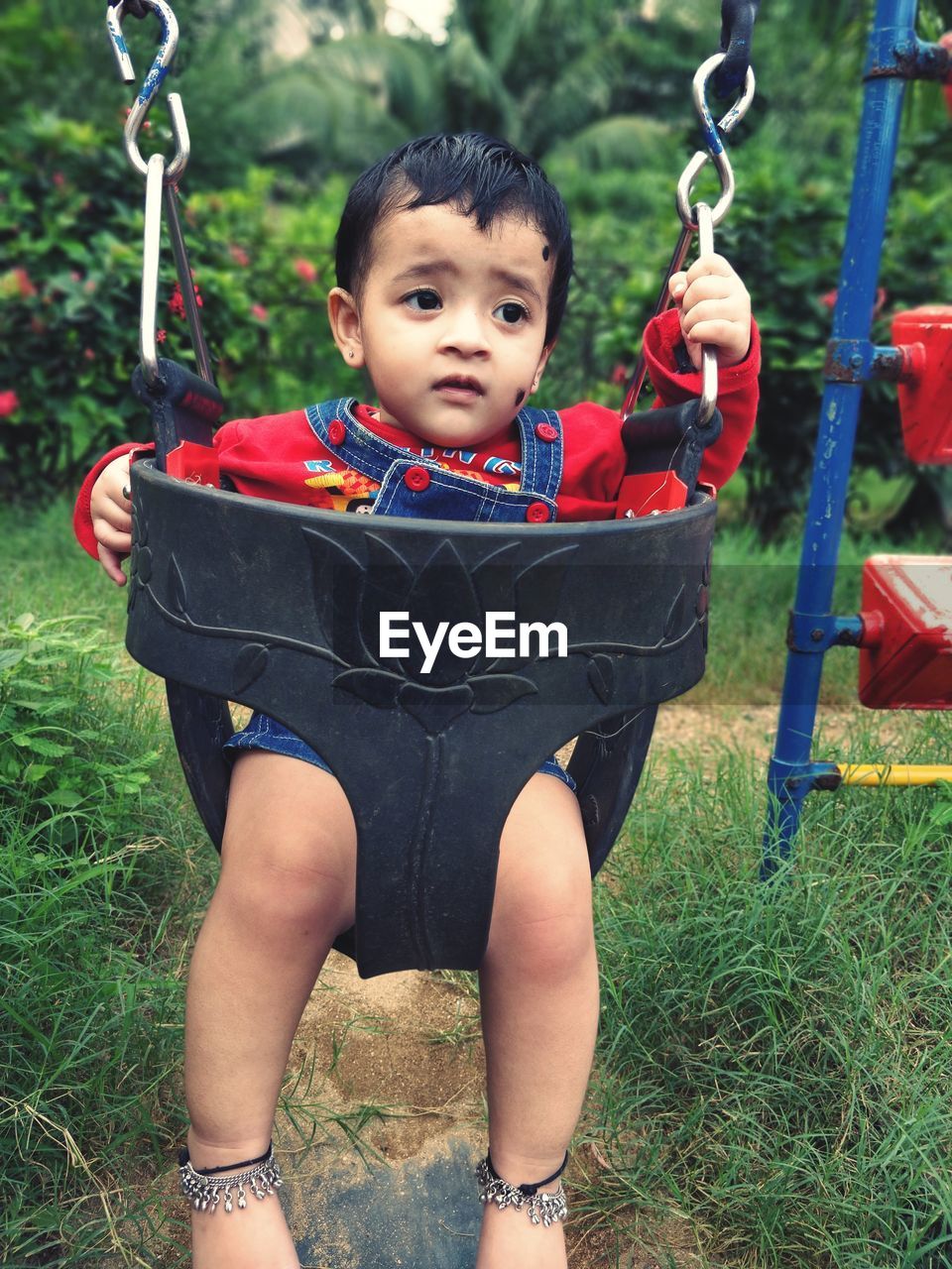 Cute girl looking away while sitting in swing at playground