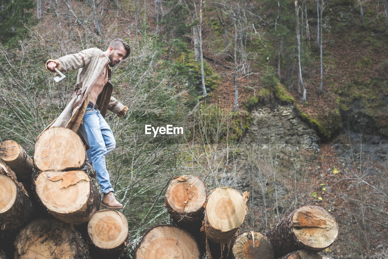 Young man walking on logs of wood in forest 